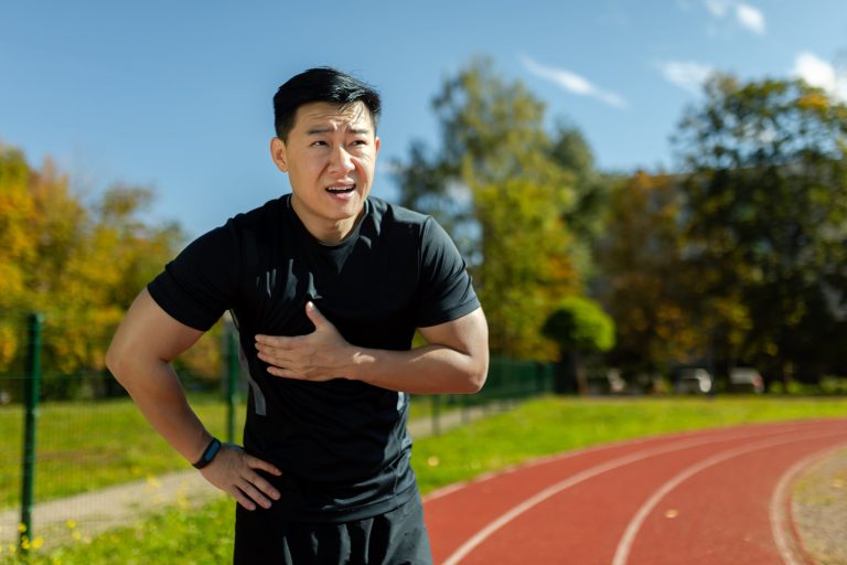 Hombre asiático en entrenamiento deportivo tiene un fuerte dolor de corazón, atleta sufre un ataque al corazón en el estadio